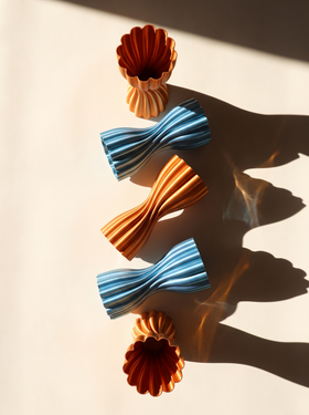 Lotus Vase Metallic in Teal Blue and Red Orange casting long shadows in warm sunlight
